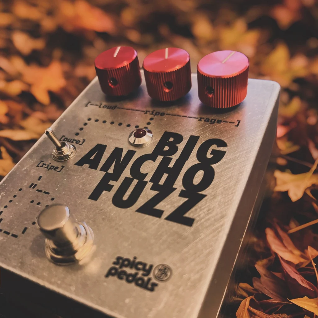 Big Ancho Fuzz photographed close up at an angle on a bed of autumn leaves, its three red knobs and the [pure] / [ripe] toggle in the foreground.