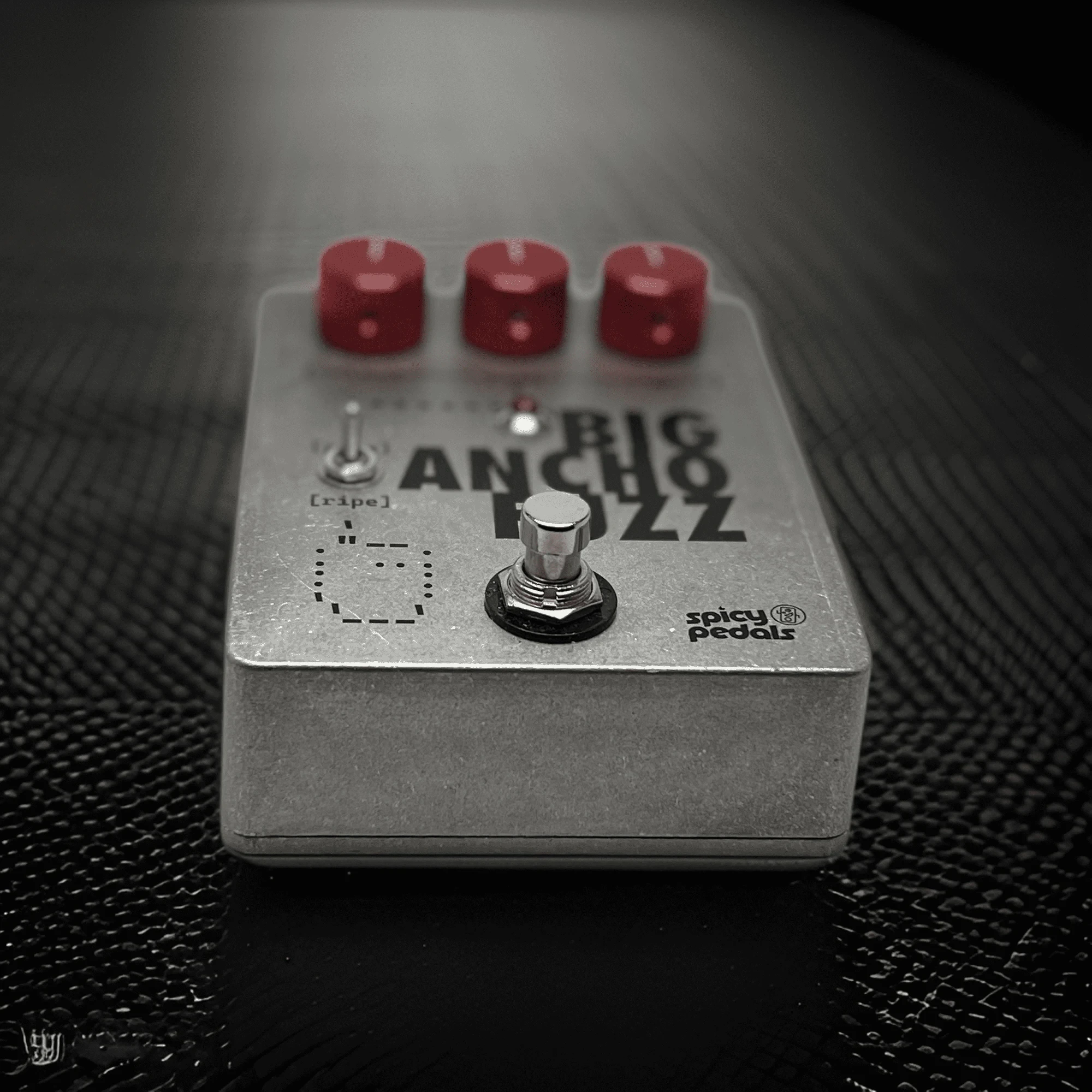 Big Ancho Fuzz lying on a dark textured surface, low angle, showing the depth of the aluminium enclosure and the side of the footswitch.