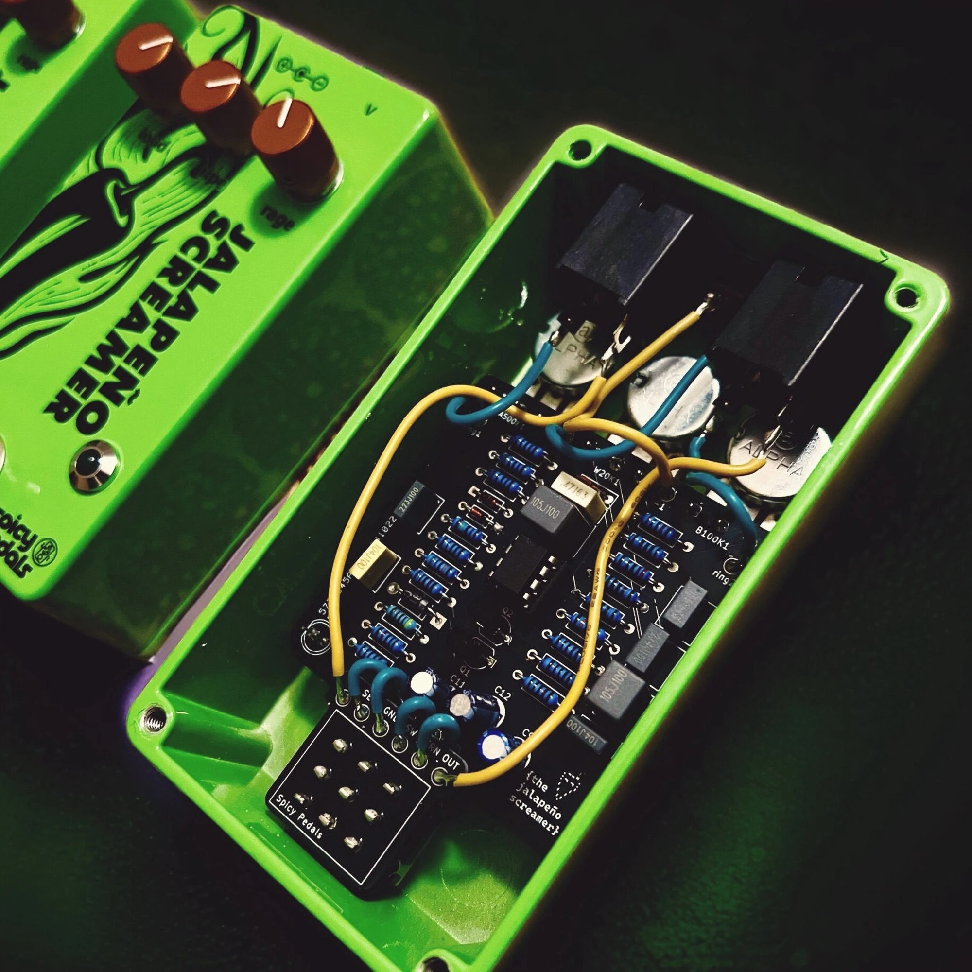 Jalapeño Screamer Verde opened up: the green enclosure lies next to its back, showing the circuit board, the hand-soldered yellow and blue wiring and the socketed chip.