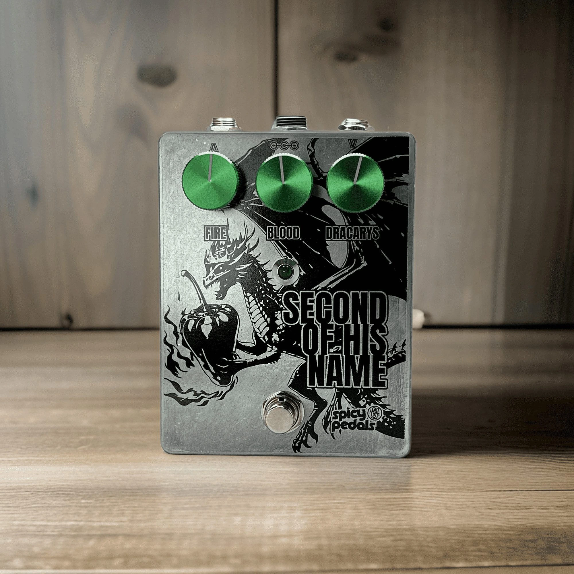 Second Of His Name standing on pale wood against a pale wooden wall, seen from three quarters, the aluminium enclosure and green knobs in even light.