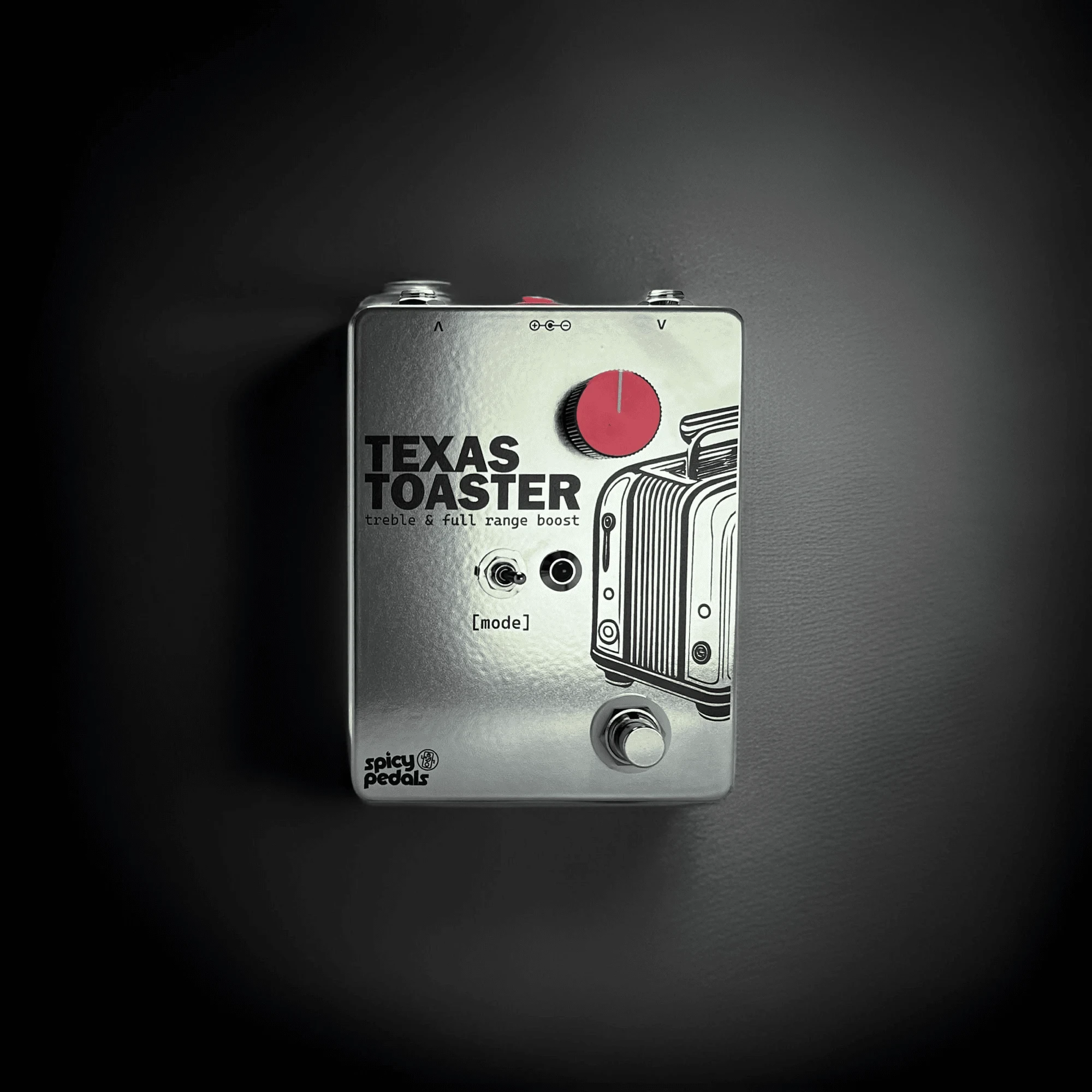 Texas Toaster on a dark ground inside a circular pool of light, seen from the front, its red knob and the toaster line drawing standing out against the darkness.