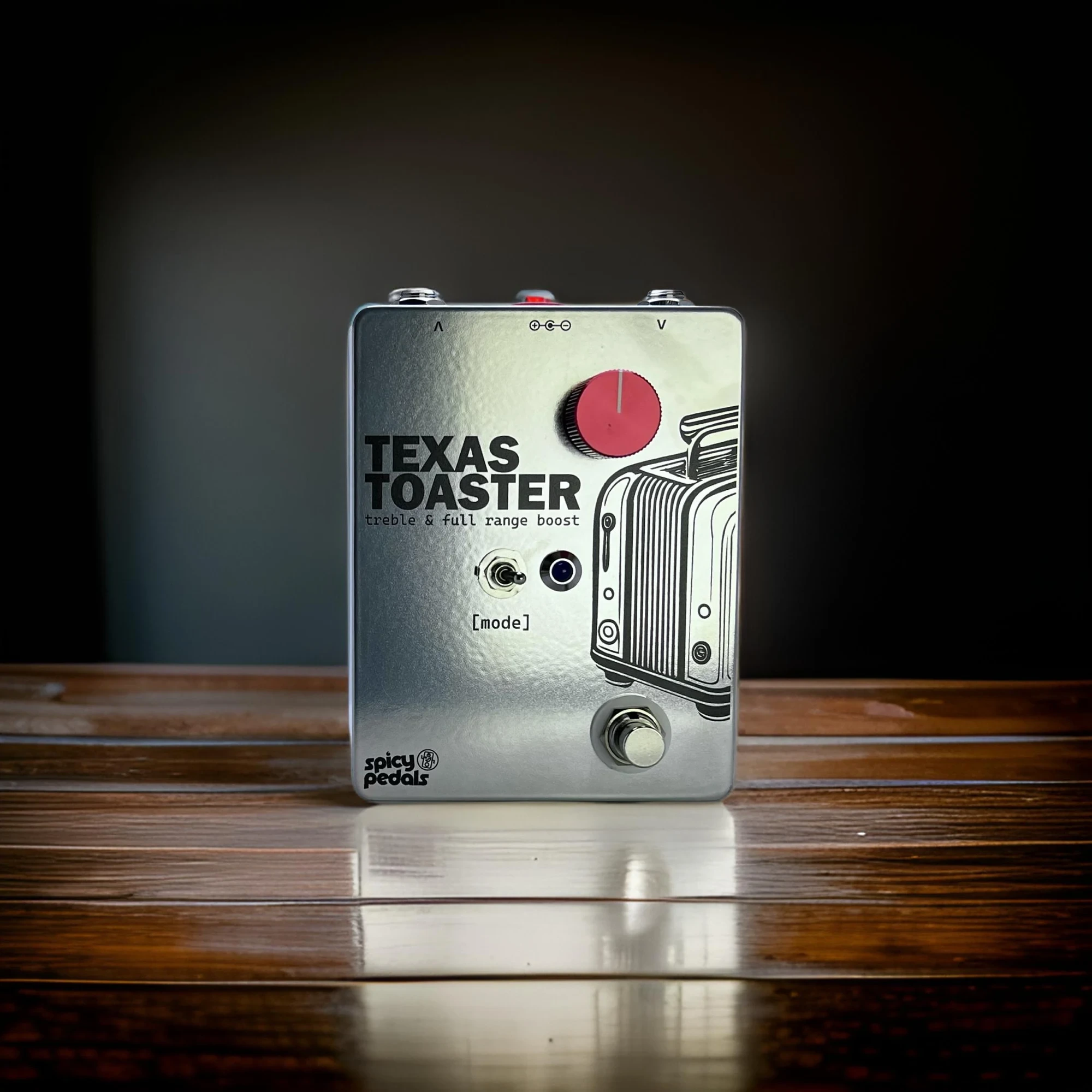 Texas Toaster standing on dark polished wood with its own reflection below it, seen from the front, red knob and [mode] switch in view.
