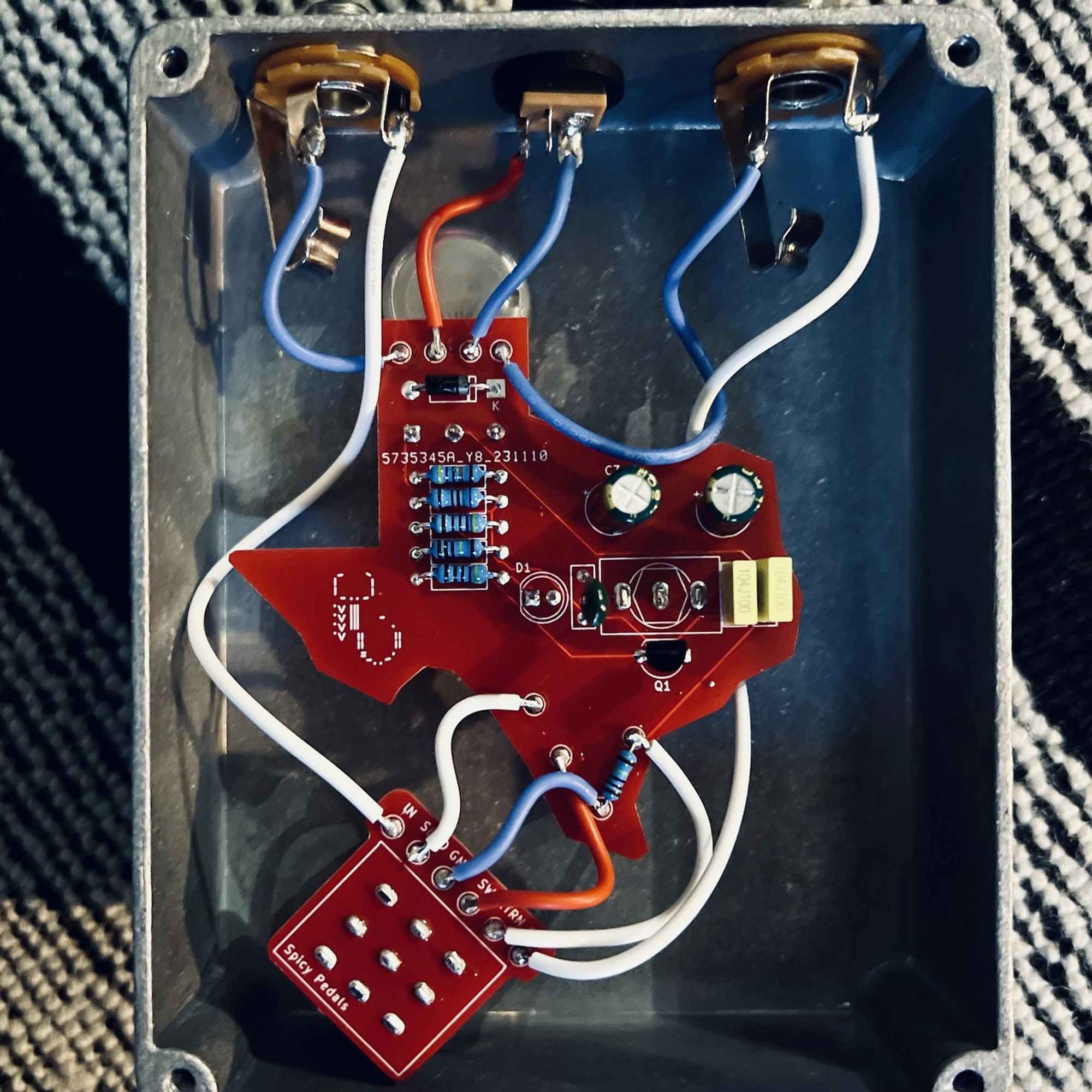 Texas Toaster opened up, seen from above: the red Texas-shaped circuit board wired point to point in white, red and blue to the jacks and pots inside the aluminium enclosure.