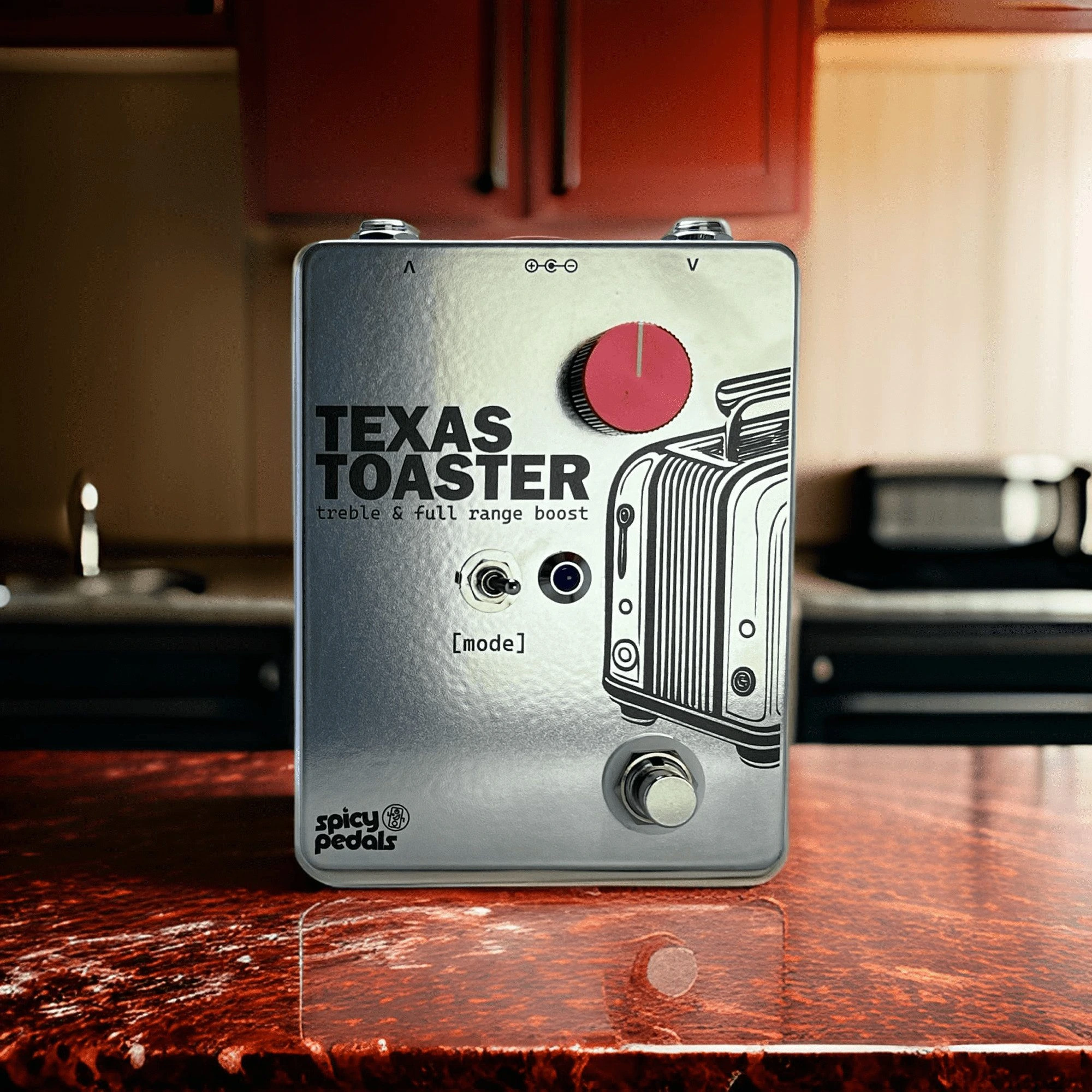 Texas Toaster on a worktop in a room with a red cabinet behind it, seen from three quarters, the red knob and the toaster artwork facing the camera.